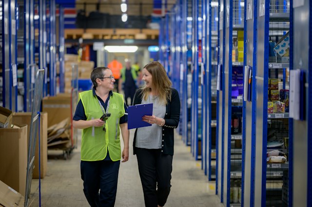 Deux professionnelles échangent dans les allées d’un entrepôt.